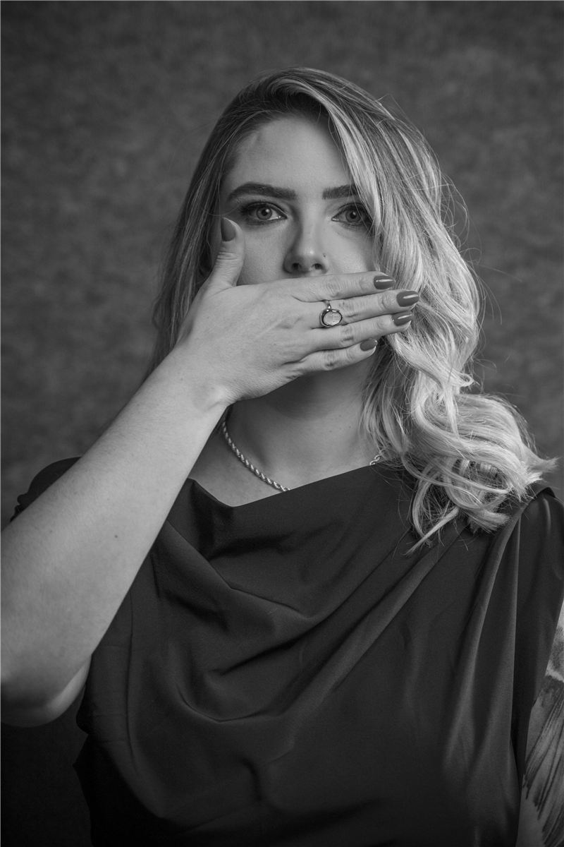 Raphaela Spellmeier em preto e branco, com a mão cobrindo a boca
